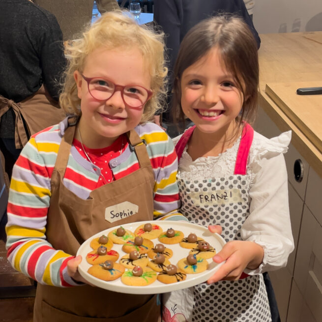 Glueckliche Kinder mit selbst gebackenen Spinnencookies beim Halloween Kinderbackkurs im Kochstudio SchlossStudio